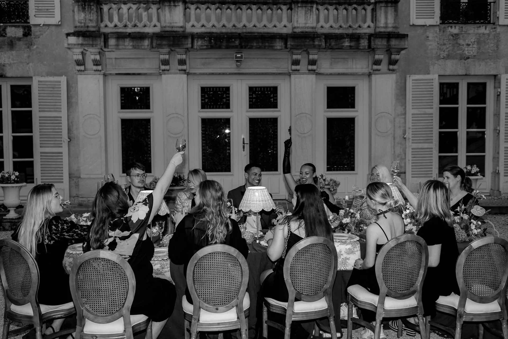 Black and white wedding guests toasting at evening reception at Chateau de Varennes in France